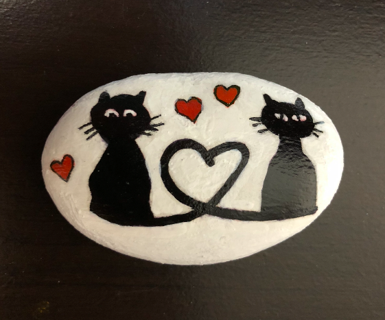 Two black cats with tails making a heart painted on a rock